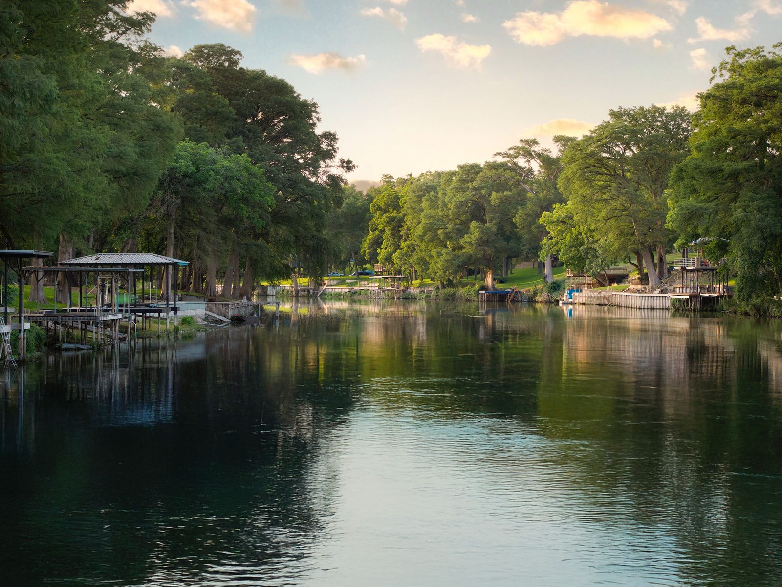 Calm water of Lake Placid at golden hour with private docks and tall trees along the shore