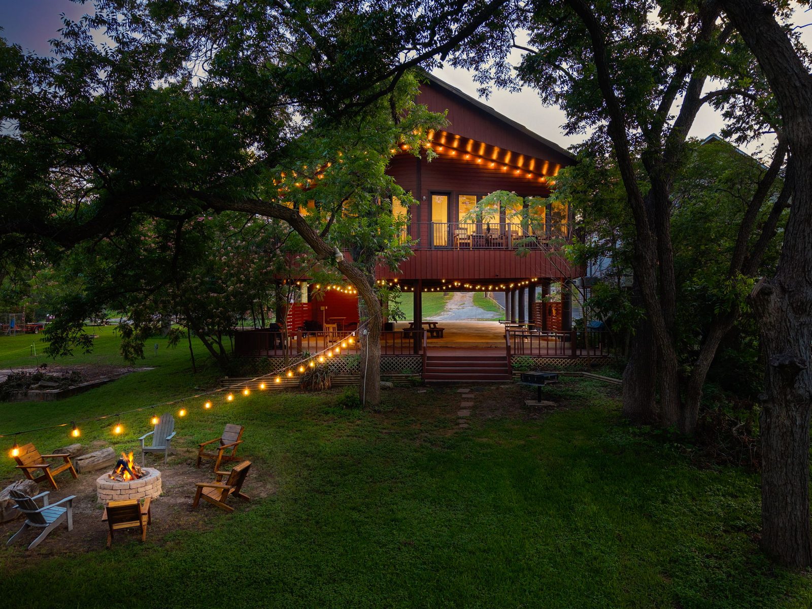 Guadalupe Lake Lodge glowing at dusk with string lights, firepit, and pecan trees